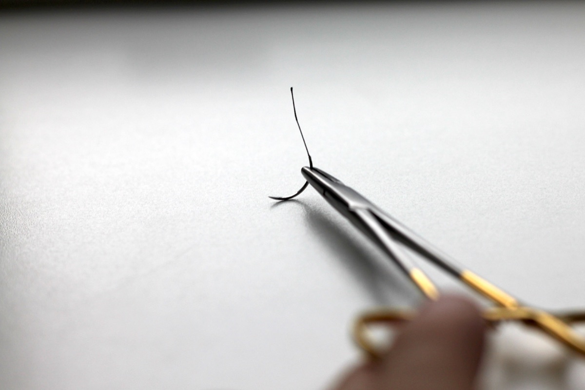 A needle holder with a curved needle mounted in the jaws