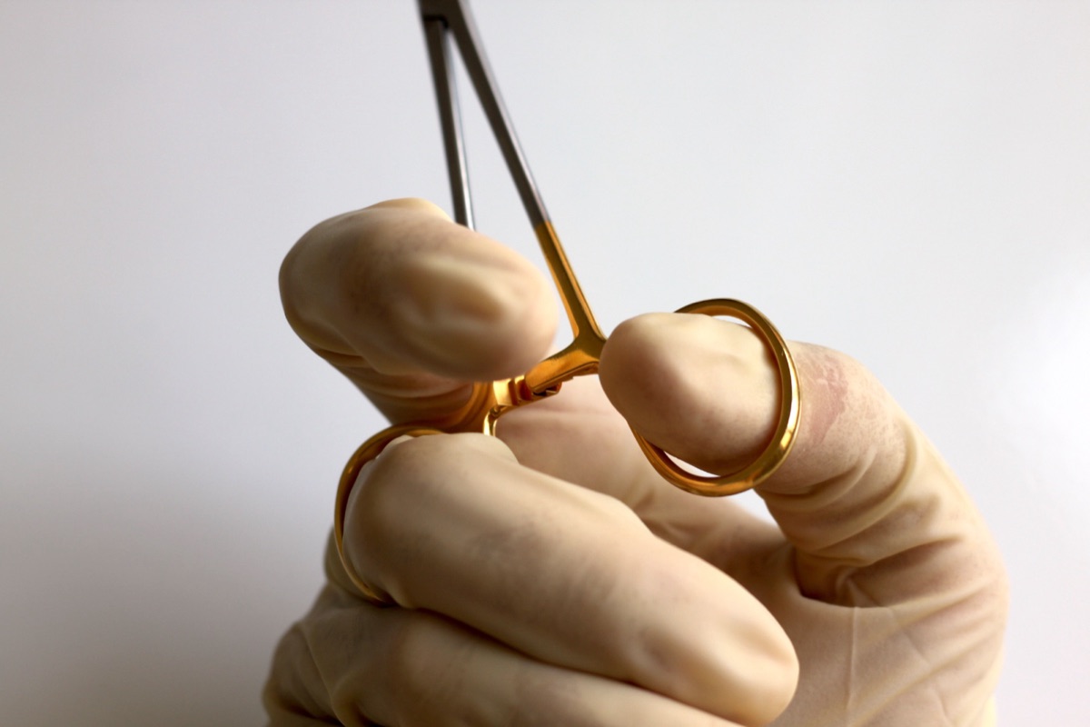 A gloved hand gripping a needle holder with the fingers pushed deep into the rings