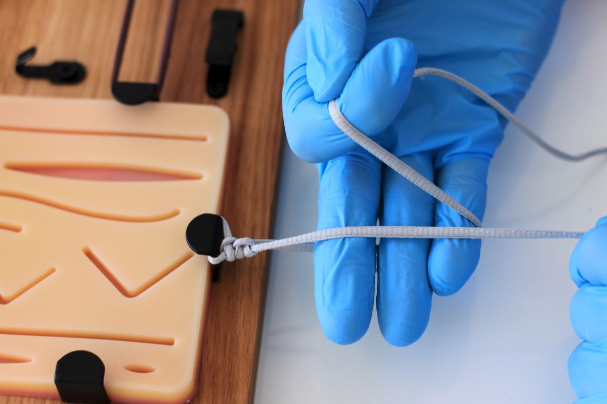 Tying a knot under tension on an elastic band stretched between hooks